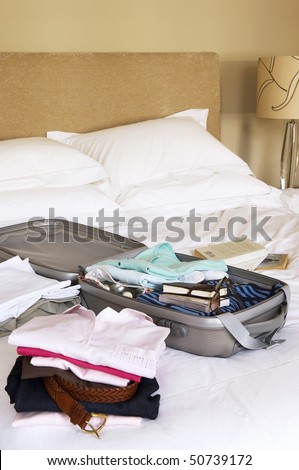 Stacks of folded clothes and packed Suitcase on Bed