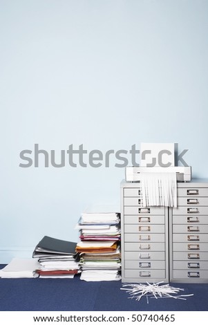 Shredder on file cabinet, stack of paperwork on floor in office