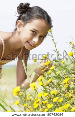 Smiling Pre-teen girl bending down, smelling flower in field of flowers