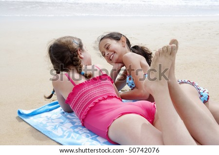 stock photo Preteen girls lying side by side on stomach on beach towel