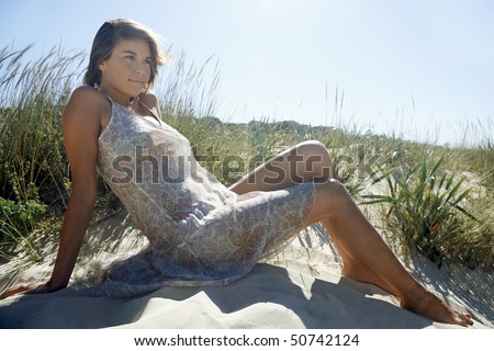 Young woman in summer dress sitting on grassy beach, side view