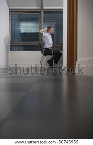 Office worker sitting with hands behind head in partly darkened office, side view