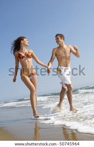 Young couple running through surf on beach, front view