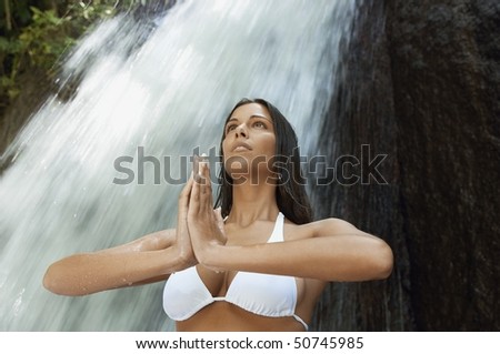 Young woman meditating by waterfall, low angle view