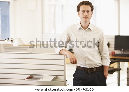Mid-adult male office worker standing by cubicle, portrait
