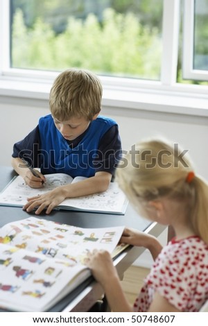 Brother and sister reading books at table at home