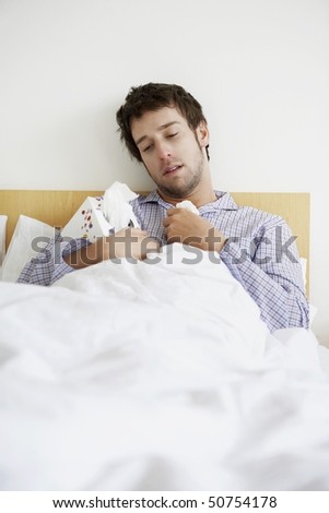 Man with cold in bed holding box of tissues