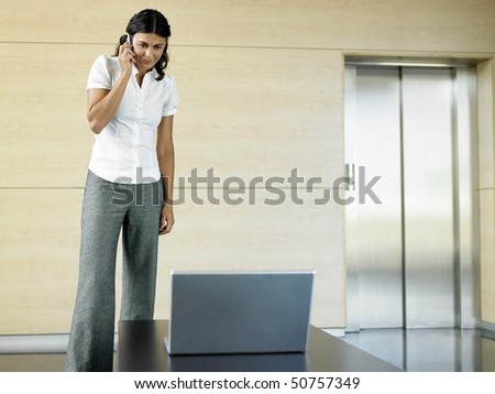 Office worker standing in lobby by laptop using cell phone