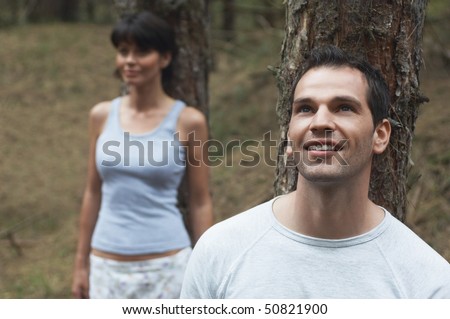 Couple in Forest Leaning on Trees, man looking up at canopy