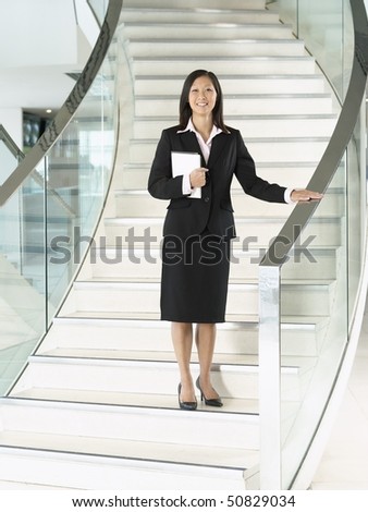 Confident Businesswomen holding folder, standing on stairs, hand on banister