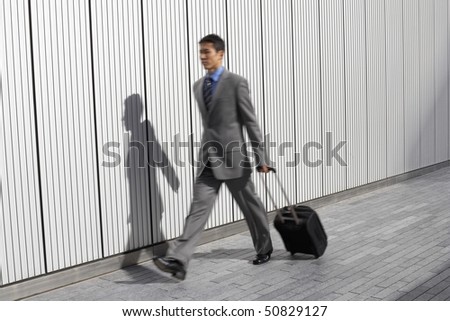 Businessman walking outdoors, pulling suitcase behind him