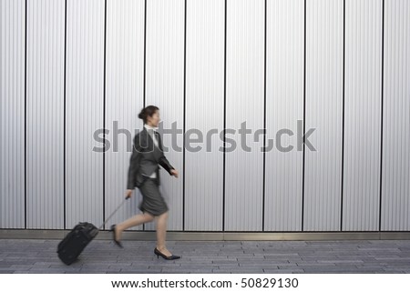 Businesswoman walking outdoors, pulling suitcase behind her, side view