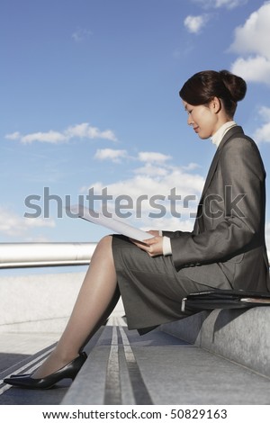Businesswoman sitting outdoor steps, reading newspaper, profile
