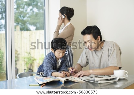 Father and Son coloring in Coloring Book on table, mother talking on mobile