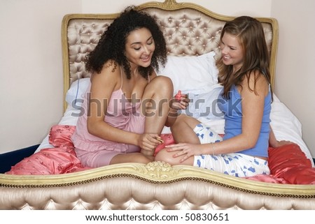 Teenage girl painting friend\'s fingernails on bed at slumber party