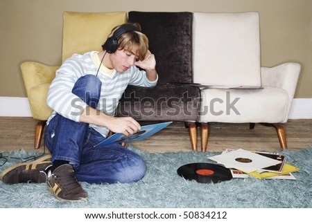 Young Man sitting on shag rug, leaning on sofa, listening to records
