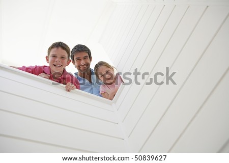 Father with son and daughter looking over white wall, view from below