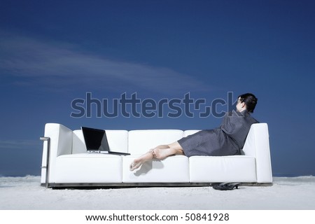 Woman reclining on sofa on beach, back view