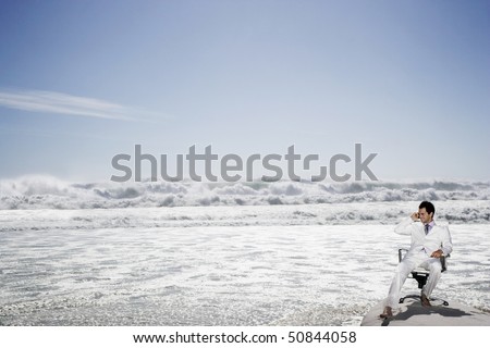 Man using mobile phone sitting on office chair on beach