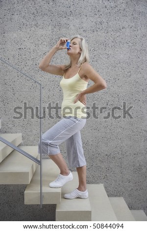 Mature woman standing, hand on hip, on stairs, using inhaler, side view