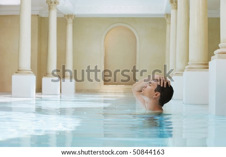 Young man with hand on head in swimming pool, side view