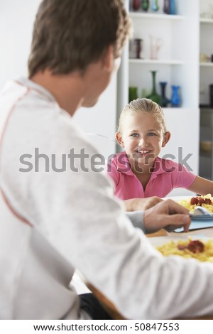 Father and daughter sitting at table eating pasta