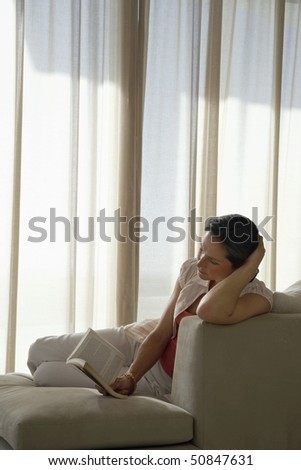 Woman reading book, reclining on sofa