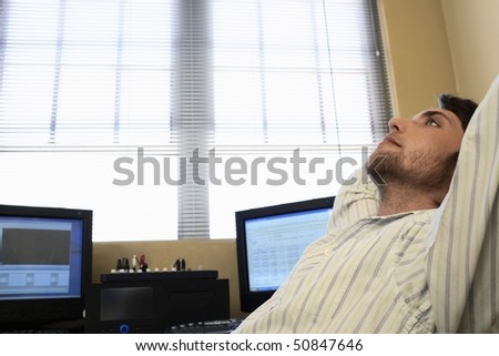 Man sitting by computers, relaxing, side view.