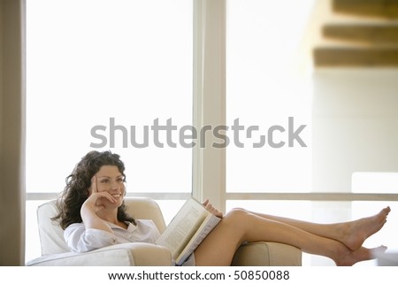 Woman holding book, sitting on armchair by window, indoors