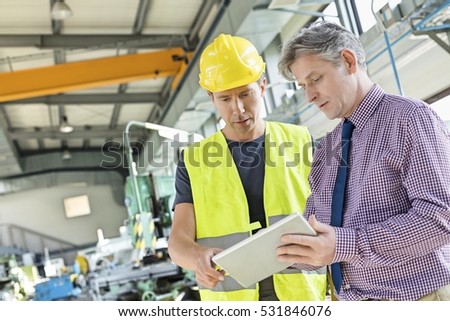 Supervisor and manual worker using digital tablet in metal industry