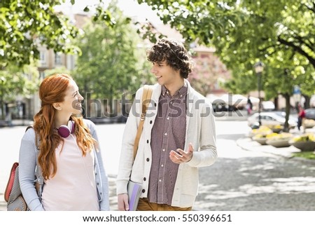 Young male and female college students talking while walking on footpath