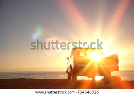 Rear view of young couple in pick-up truck parked in front of ocean enjoying sunset