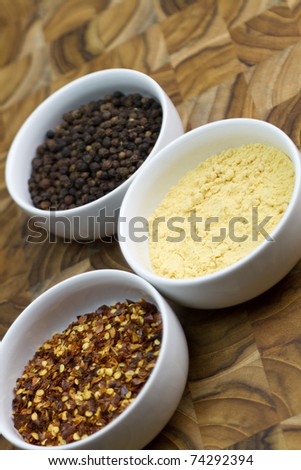Three bowls of spices on butcher block -  yellow mustard, black pepper and red pepper flakes