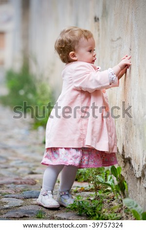 Small cute girl standing near old wall and painting graffiti
