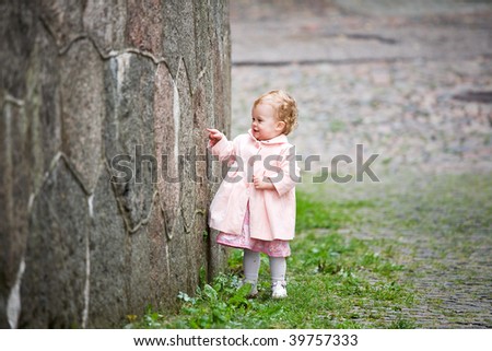 Small cute girl standing near old wall and painting graffiti