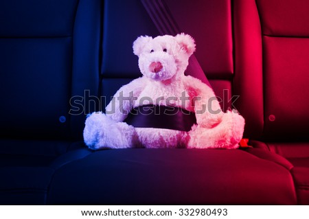 Teddy bear fastened in the back seat of a car, red and blue police lights