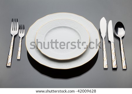 A plates and a set of silverware on grey glass table