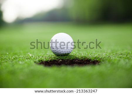 Golf ball on green meadow.  golf ball on lip of cup