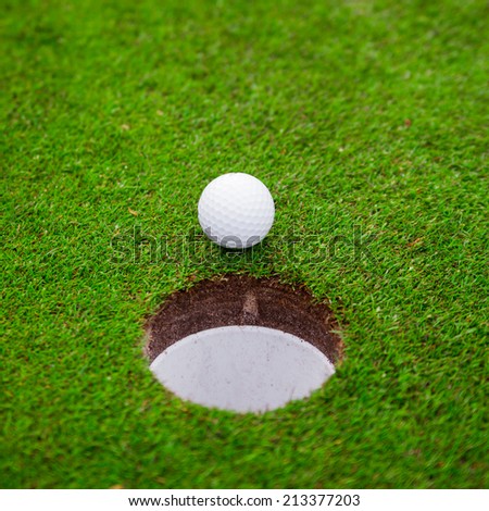 Golf ball on green meadow.  golf ball on lip of cup