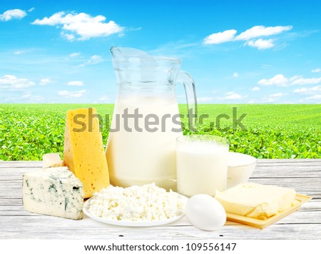 Dairy products on wooden table and field with green grass on background