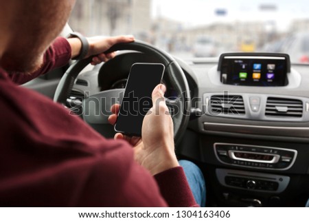 The young man sitting in his car behind the wheel and looking on his phone in his hand