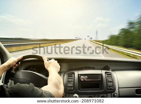 Man\'s hands of a driver on steering wheel of a minivan car on asphalt road