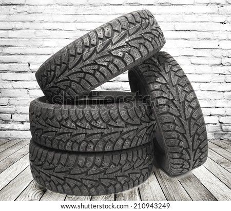 Stack of four new black tyres for winter car on  wooden floor in vintage room with brick wall background