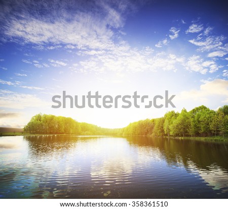 View of the lake with green coast and clouds and bright sun