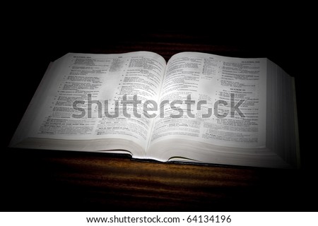 One open bible on table in black background