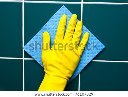 Hand with yellow sponge cleaning the bathroom tiles
