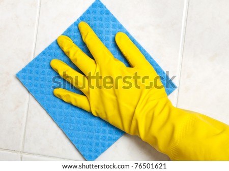 Hand with yellow sponge cleaning the bathroom tiles