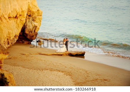 Bride and groom standing on the beach by the beautiful caves and looking at each other.