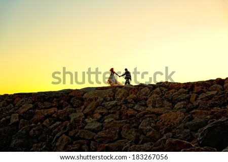 Bride and groom walking on the rocks by the ocean. Romantic moment at the sunset.