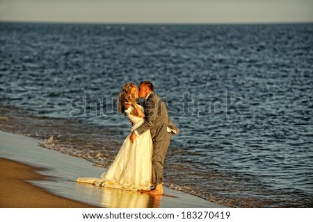 A married couple, bride and groom, kissing on a beautiful beach.